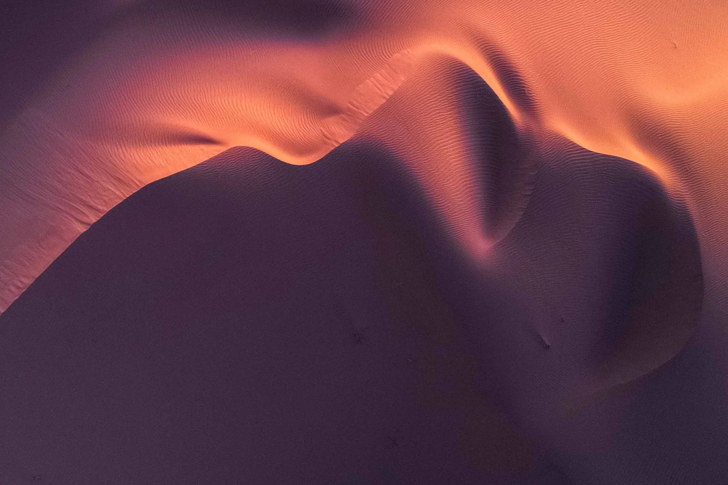 Drone aerial of sculpted sand dunes at twilight with soft pink and purple tones across the ridgelines