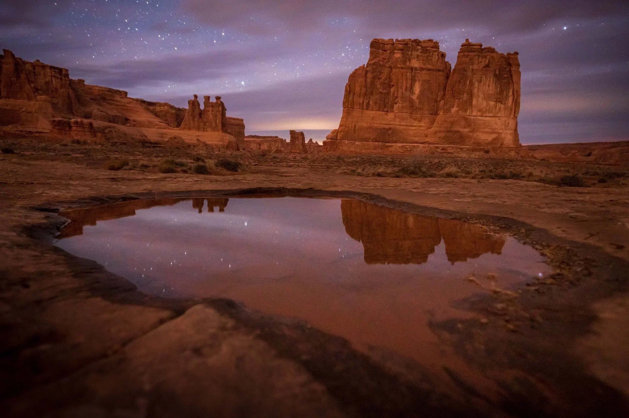Desert rock formations reflected in a rain-filled pothole under a starry sky in Arches National Park, Utah