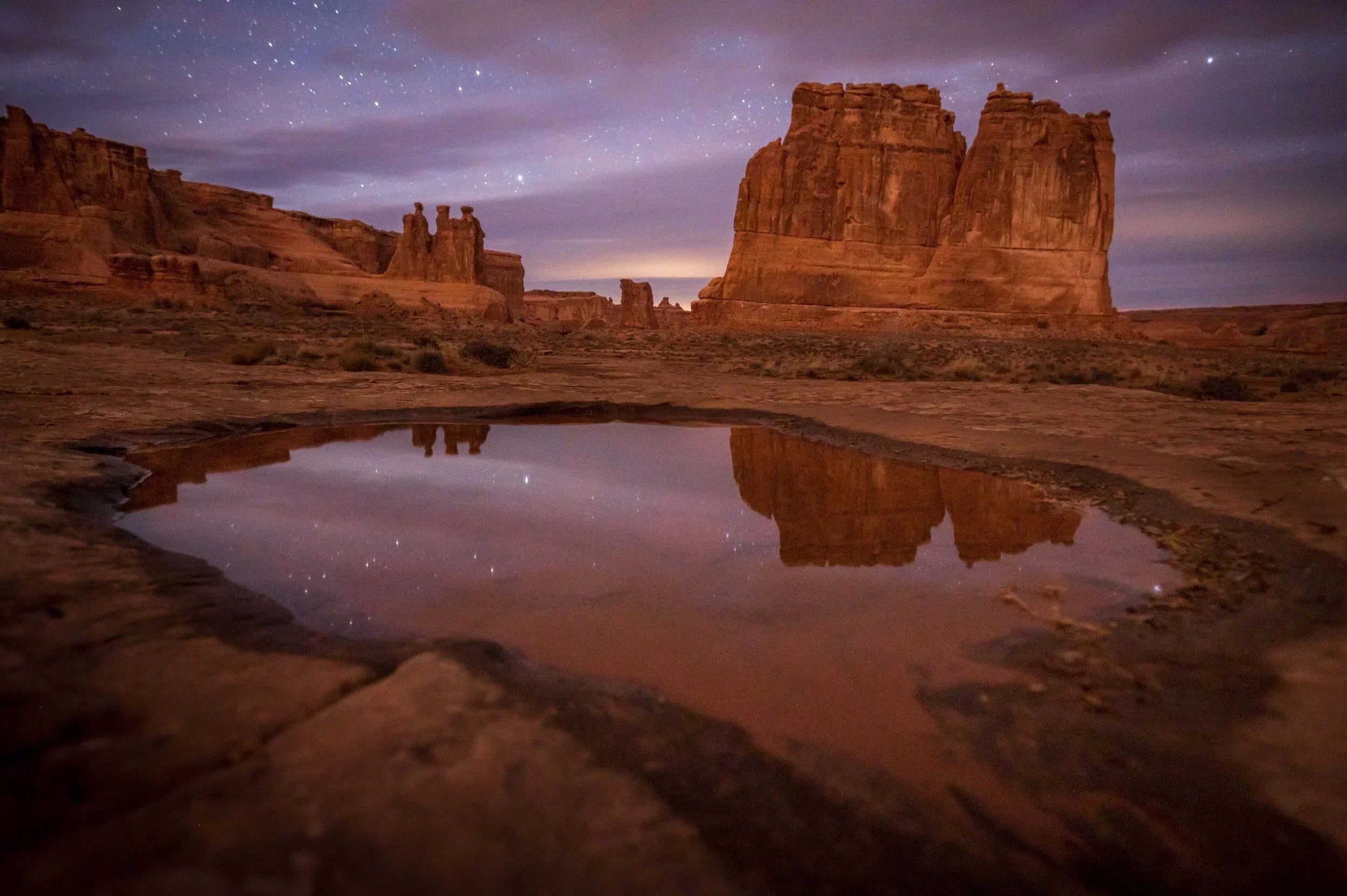 Desert rock formations reflected in a rain-filled pothole under a starry sky in Arches National Park, Utah