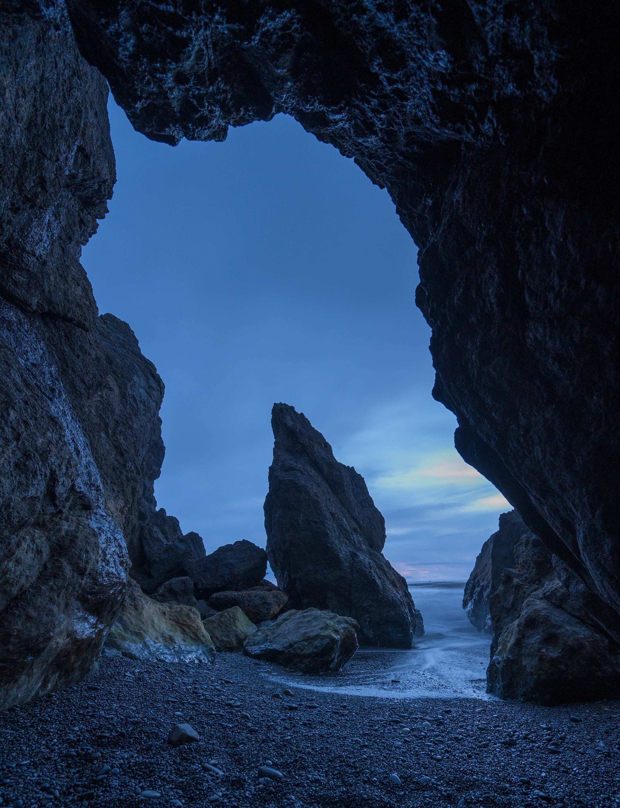 Sea stack framed by coastal rock cave at dusk in Olympic National Park, Washington