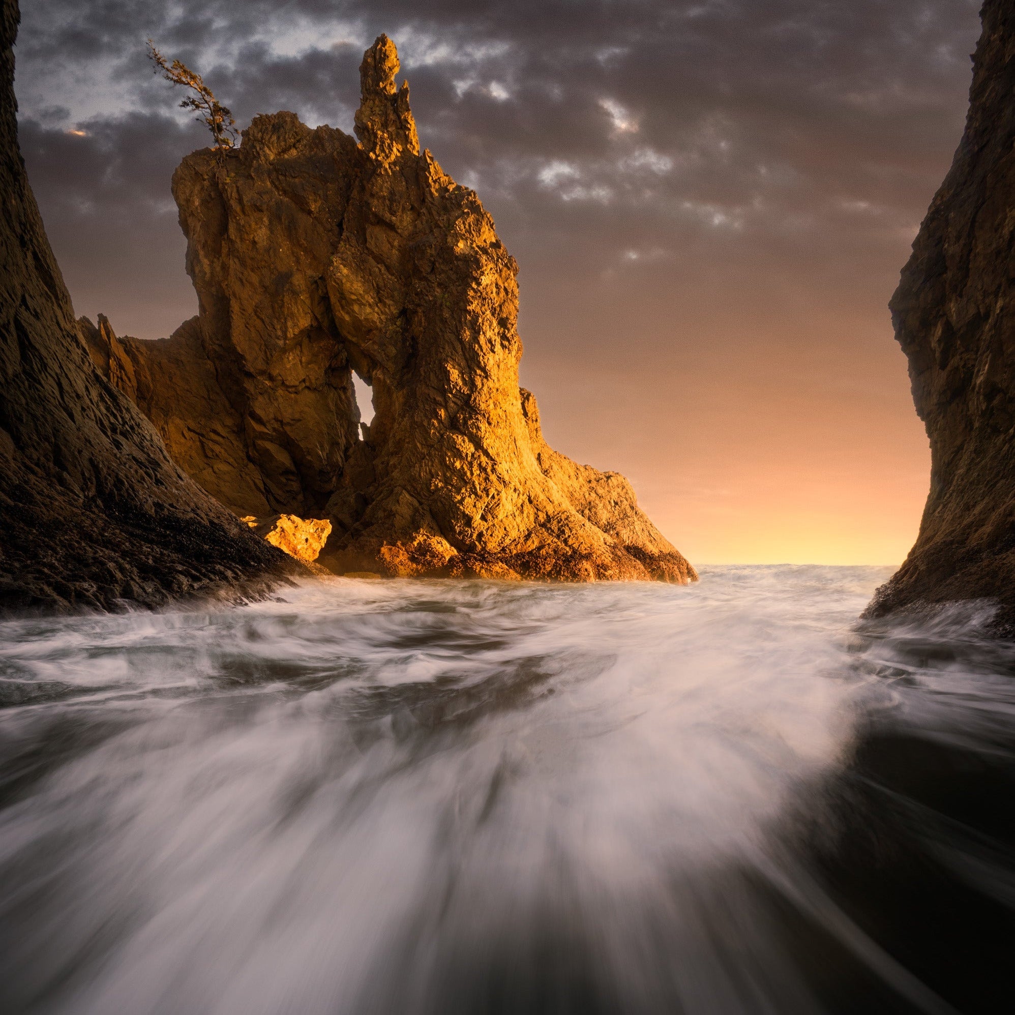 Long exposure ocean waves flowing around rocky sea stacks at sunset along a rugged coastline