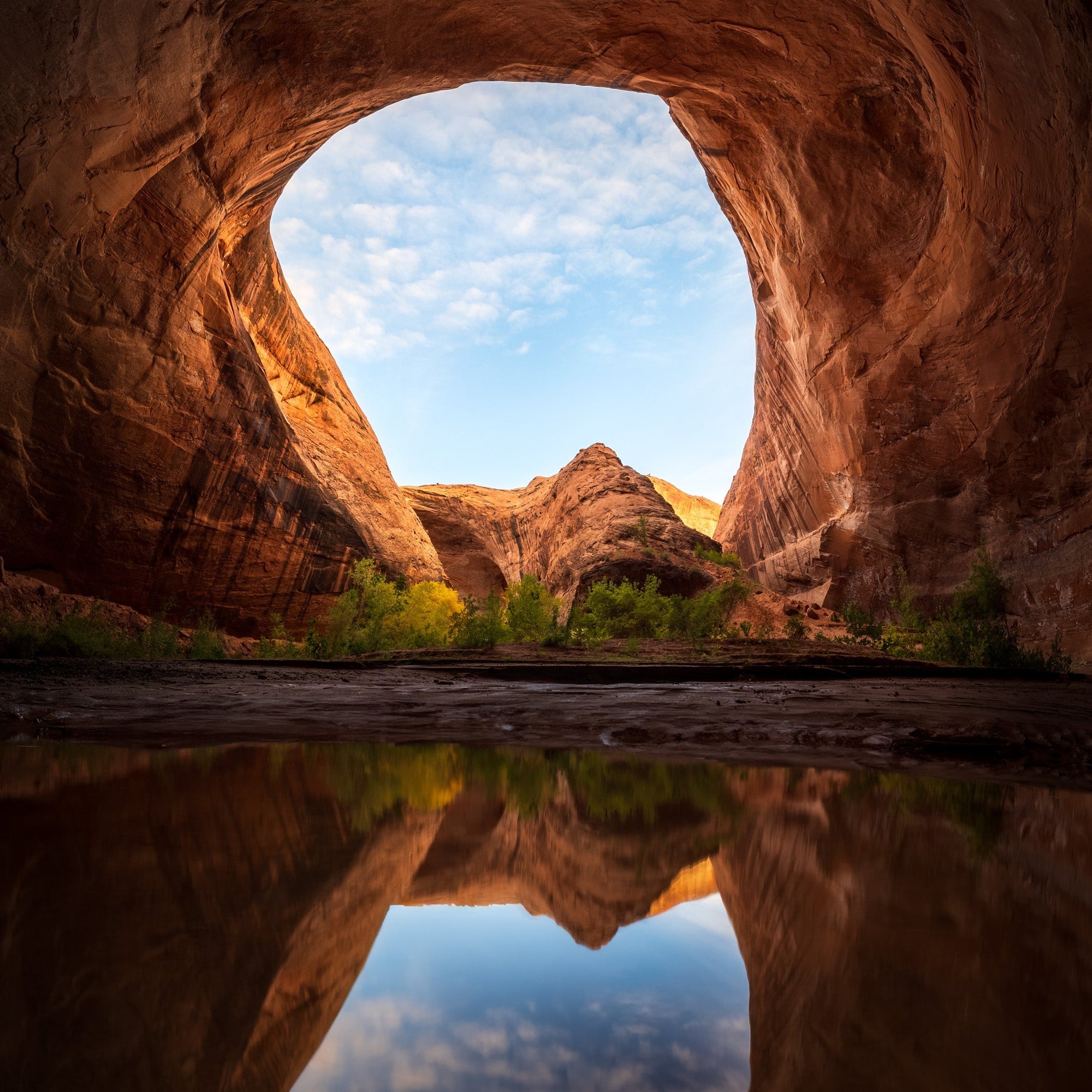 Natural sandstone arch in Utah desert framing canyon landscape and reflection at sunrise in the American Southwest