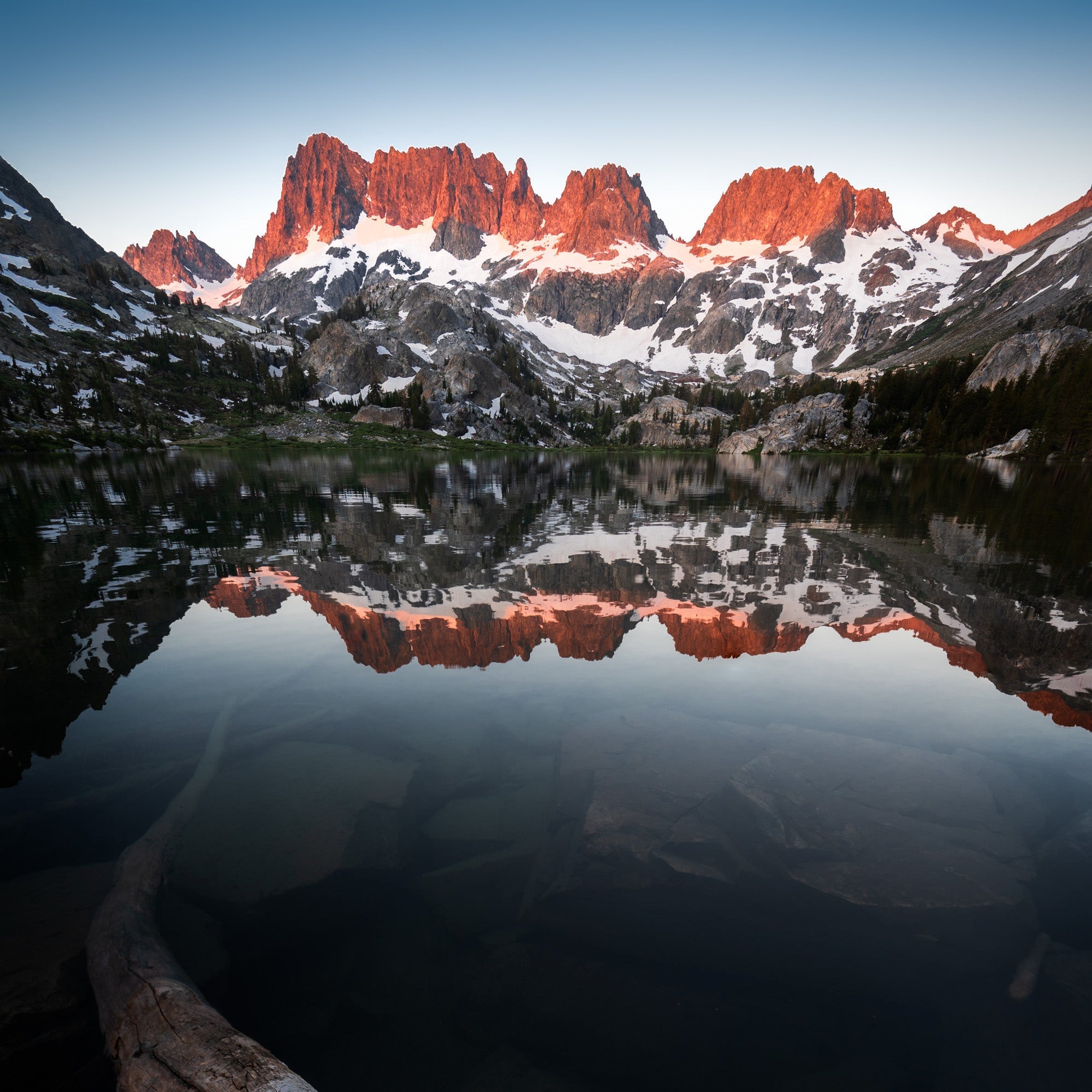 Snow-covered mountain range reflected in alpine lake at sunrise, dramatic high-altitude wilderness landscape