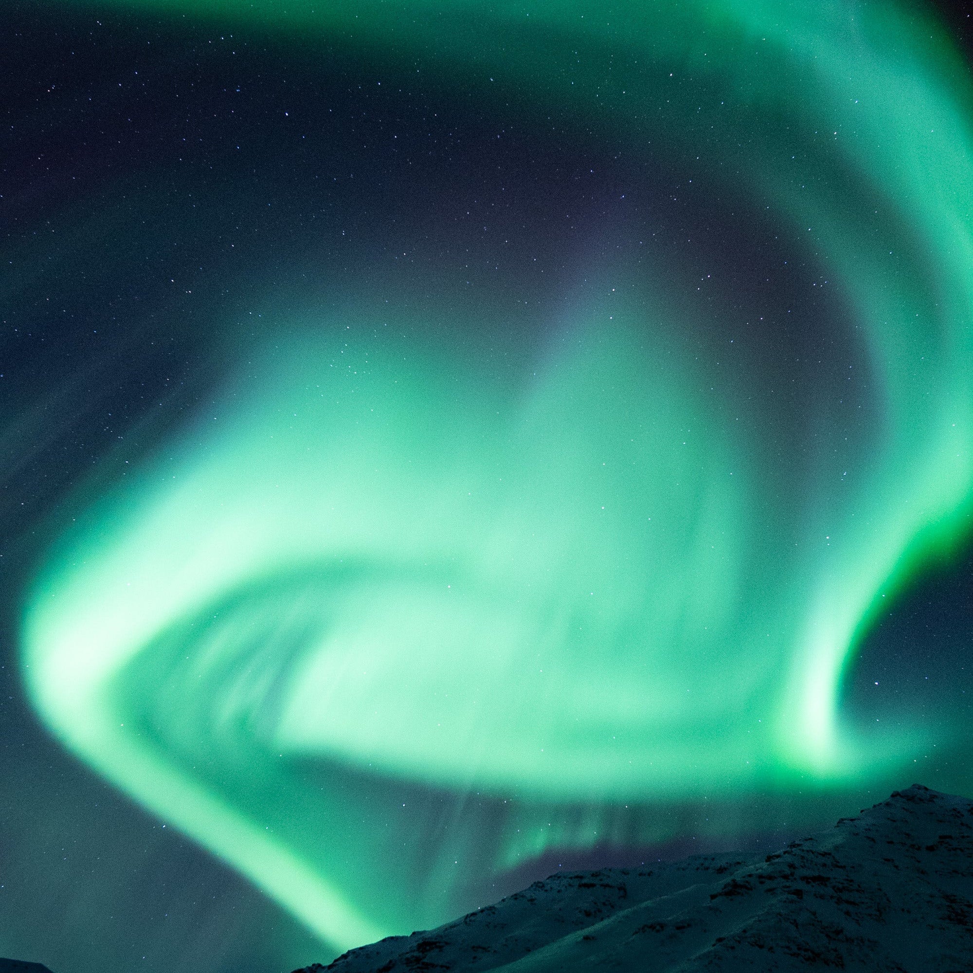 Aurora borealis spiral over snow-covered mountains under a starry winter night sky