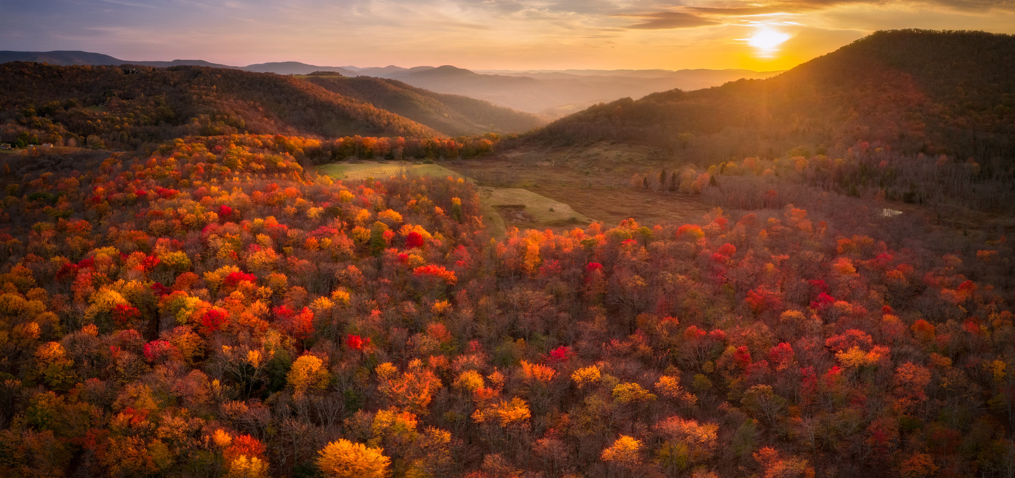 Fiery fall foliage covering rolling hills near Canaan Valley, West Virginia, glowing orange and red at sunset.