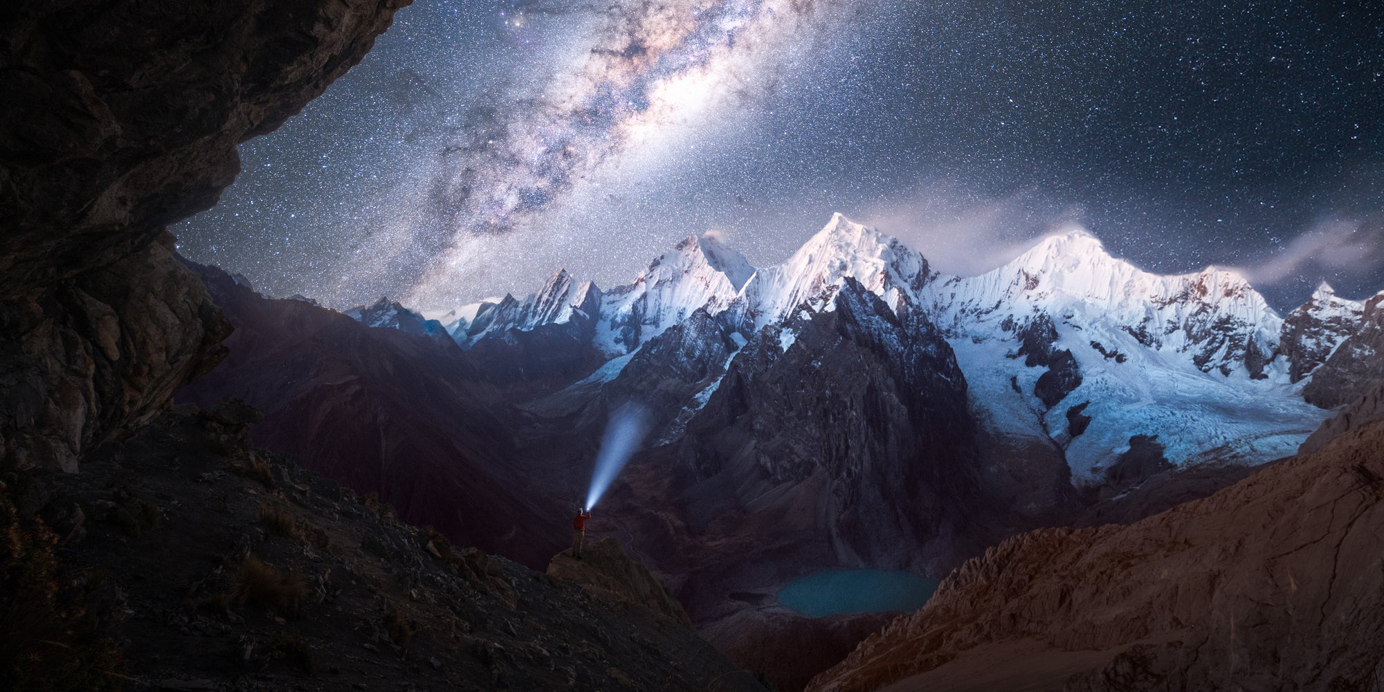 Panoramic night view of the Cordillera Huayhuash mountains in Peru, with snow-covered Andean peaks beneath the Milky Way and a lone hiker’s headlamp glowing below.