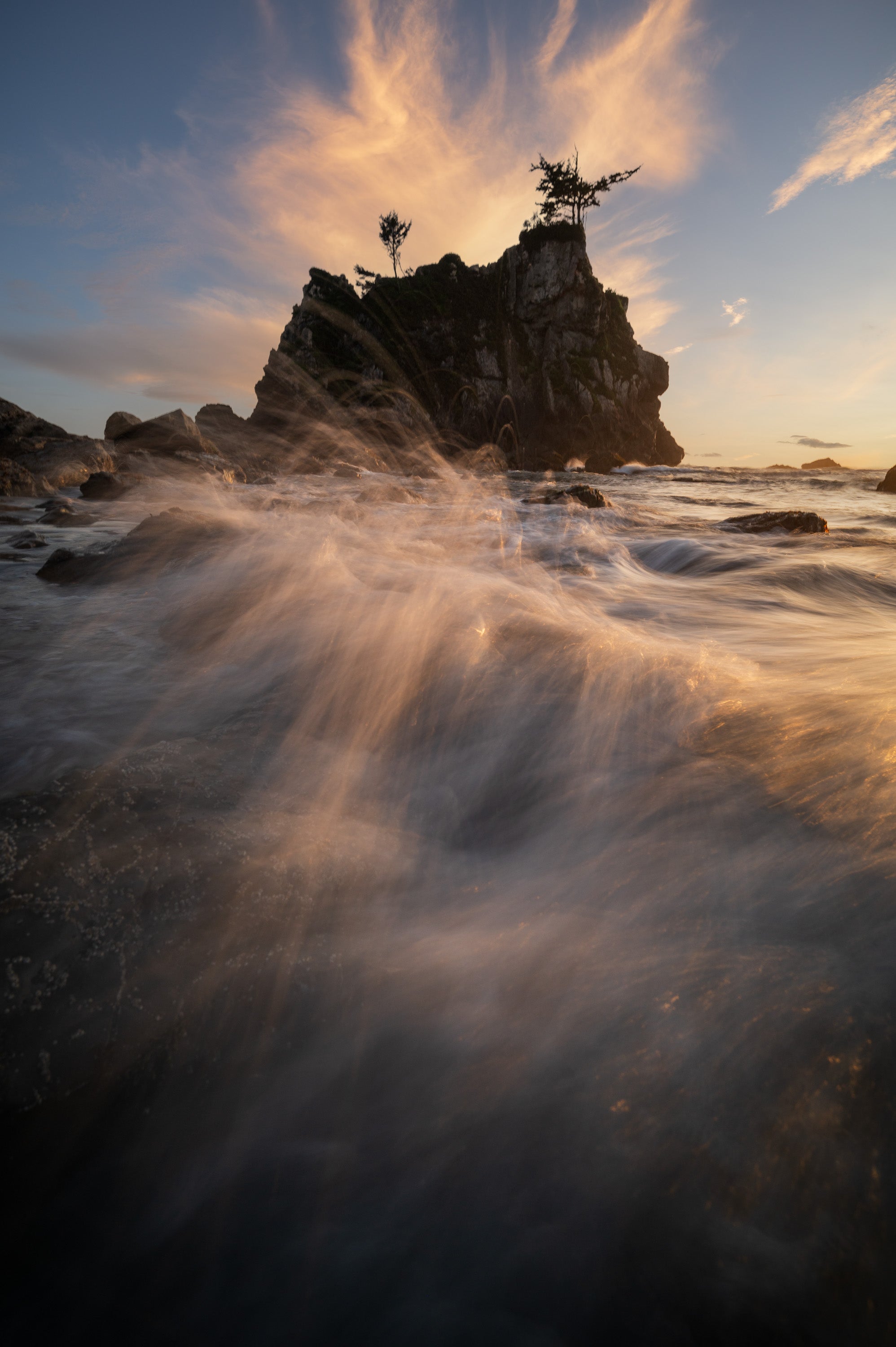 Long-exposure coastal photograph near Klamath, California, showing waves breaking against rocky shoreline and sea stacks glowing in warm evening light.