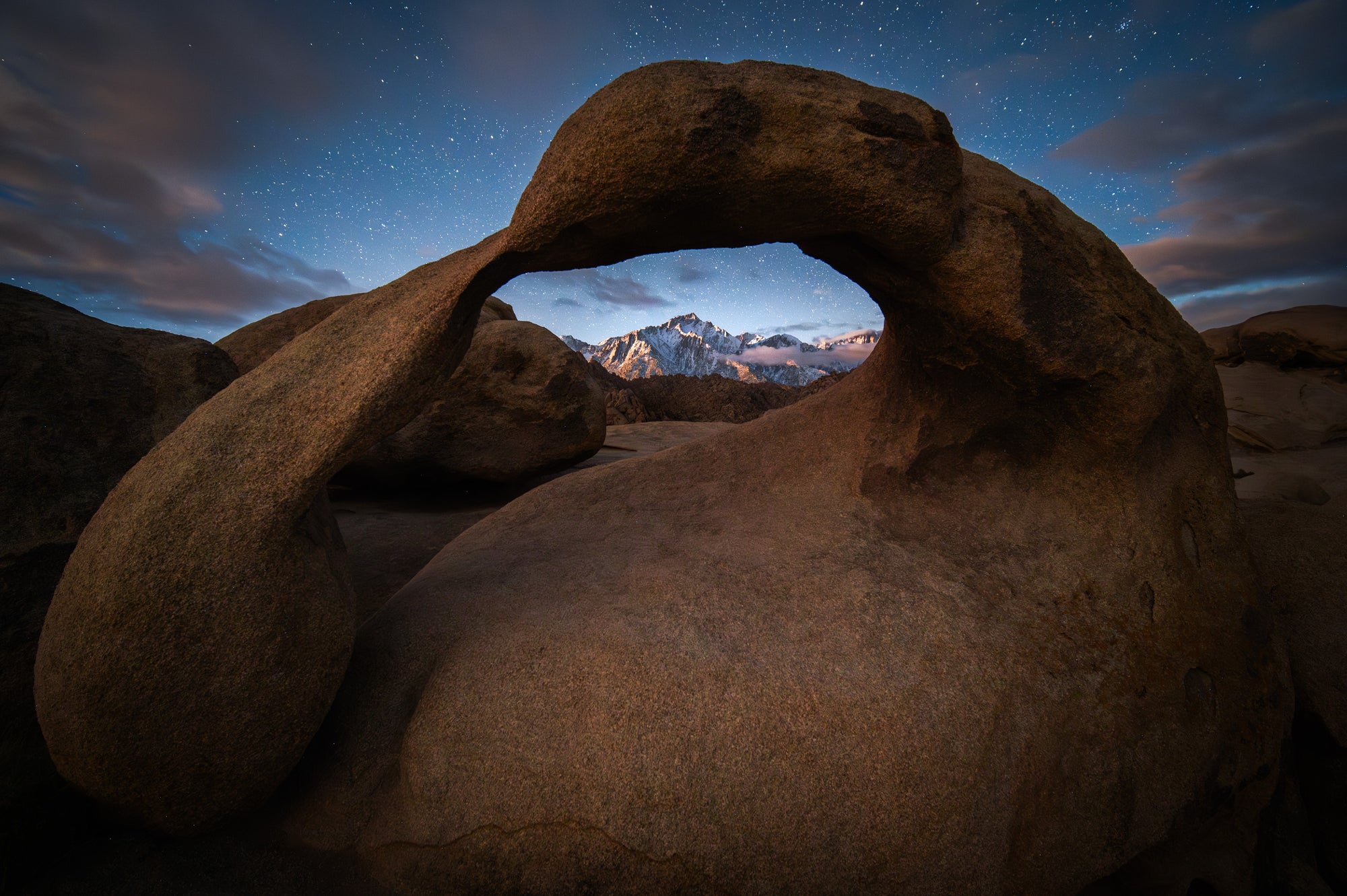 Mobius Arch in the Alabama Hills framing Lone Pine Peak at moonrise, with warm light on the Sierra Nevada and stars visible in the night sky.