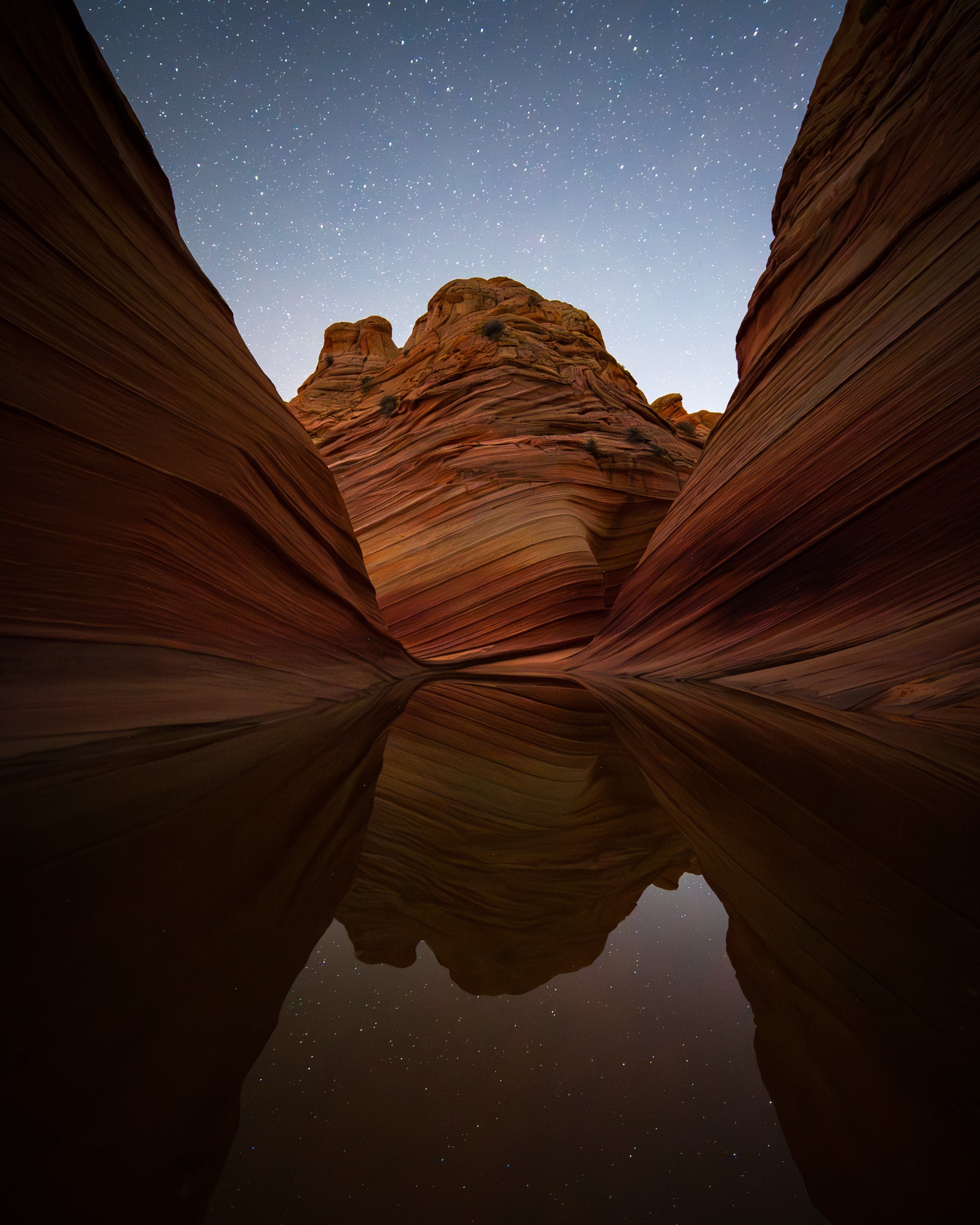 Sandstone walls of the Wave reflected in still water at night under a star-filled sky on the Arizona–Utah border