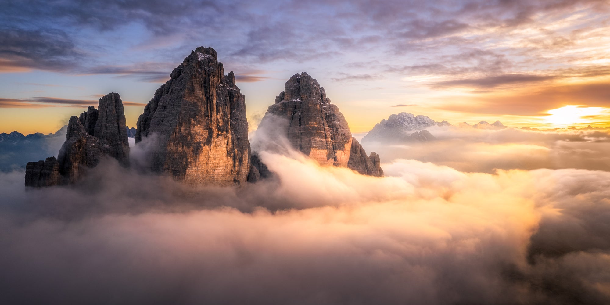 Tre Cime di Lavaredo rising above golden clouds at sunset in the Italian Dolomites