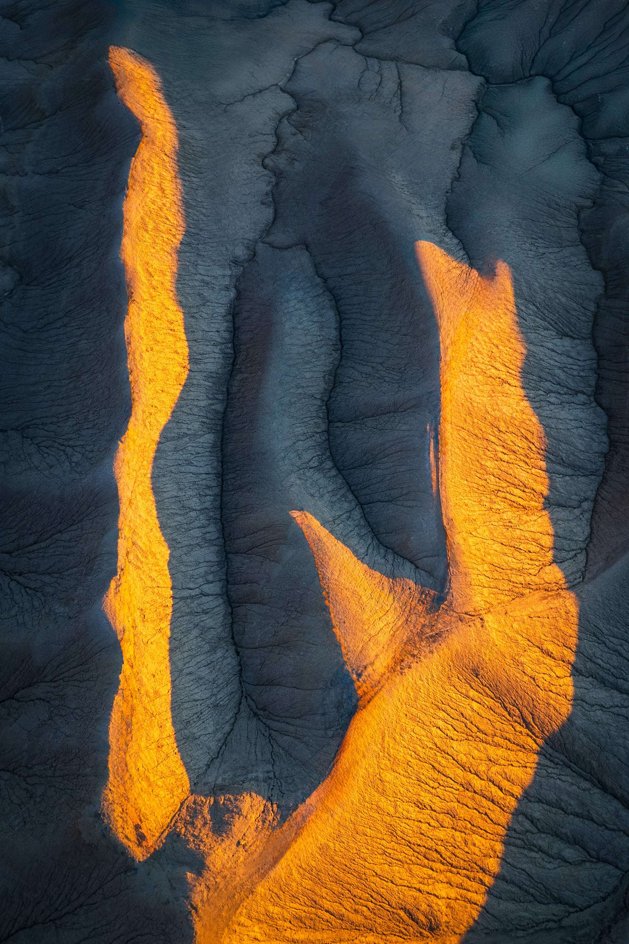 Aerial abstract of Utah badlands at sunrise, with blue-toned clay ridges intersected by bright orange sunlight on the ridge tops.